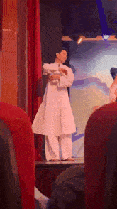 a man in a white robe is standing on a stage in front of a red curtain