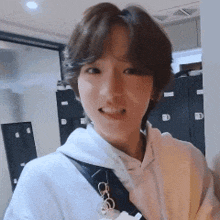 a woman with short hair is wearing a white hoodie and a black strap around her shoulder .