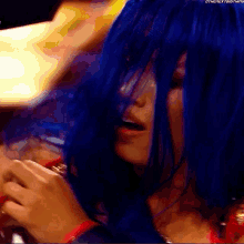 a woman with blue hair is wearing a red top and a red necklace .