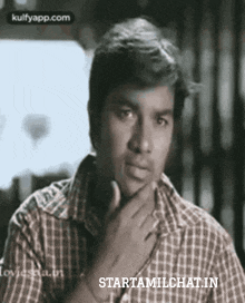 a man in a plaid shirt is holding his hand to his chin and looking at the camera .