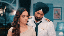 a man in a turban and tie stands next to a woman in a white dress