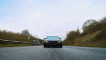 a black car is driving down a highway with a few trees in the background