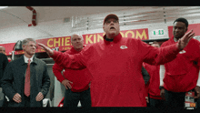 a man in a red jacket stands in front of a sign that says chiefs kingdom