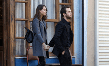 a man in a suit and a woman in a gray coat hold hands
