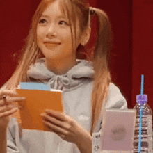 a woman in a hoodie is holding a book and a bottle of water .
