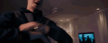 a man in a black jacket is dancing in front of a tv