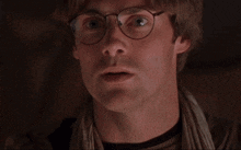 a close up of a man 's face with glasses and a scarf around his neck