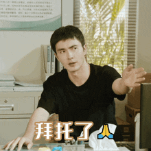 a man in a black shirt is sitting at a desk in front of a window