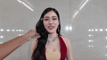 a woman wearing a red dress and a necklace smiles while a man touches her hair