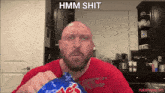 a bald man in a red shirt is holding a bag of m & ms