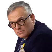 a man wearing glasses and a blue suit looks to his right
