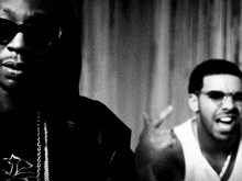 a black and white photo of two men one wearing sunglasses and the other wearing a white tank top