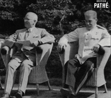 a black and white photo of two men sitting in chairs with pathe written on the bottom right