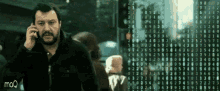 a man with a beard is talking on a cell phone in front of a screen that says mq
