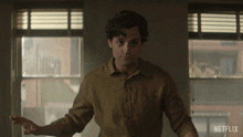 a man in a brown shirt is standing in front of a window with netflix written on the bottom right