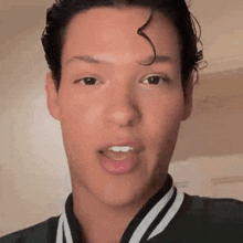 a close up of a man 's face with his mouth open and a black and white jacket on .