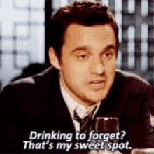 a man in a suit and tie is sitting at a table with a glass of wine .