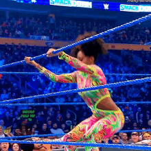 a woman in a colorful outfit is jumping through a wrestling ring