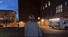 a man is walking down a street with a food truck parked in front of a building