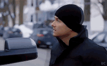 a man wearing a black hat is standing in front of a car with the word uc on the bottom right