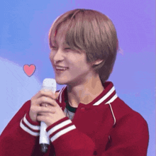 a young man in a red jacket is holding a microphone and smiling with a heart above him .