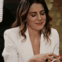 a woman in a white jacket is smiling while holding a pen and a cell phone .