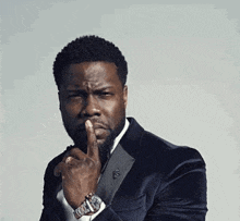 a man in a suit and tie is making a silly face while holding his finger to his mouth .