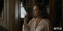 a woman wearing glasses stands in front of a bookcase with netflix written on the bottom