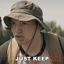 a man wearing a hat and a backpack says " just keep "