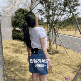 a woman in a white shirt and denim shorts is standing in front of a road
