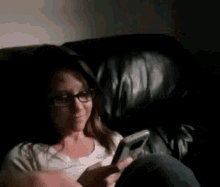 a woman with glasses is sitting on a couch looking at her phone
