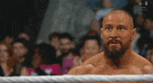 a man with a beard is standing in a wrestling ring with a crowd in the background .