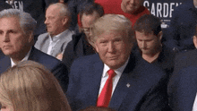 donald trump is sitting in a crowd of people wearing a suit and tie