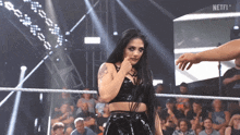 a woman stands in a wrestling ring with the word netfi on the screen behind her