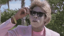 a man wearing a pink suit and sunglasses is making a face .