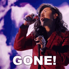 a man in a red suit singing into a microphone with the word gone behind him