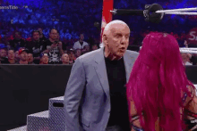 a man in a suit and a woman with pink hair are standing in a wrestling ring .