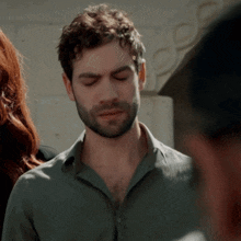 a man with a beard wearing a green shirt looks down with his eyes closed