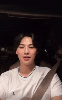 a young man wearing a white polo shirt is sitting in a car at night