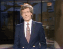 a man in a suit and tie is standing in front of a glass door in a dark room .