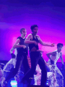 a man in a black tank top is dancing on a stage with other men