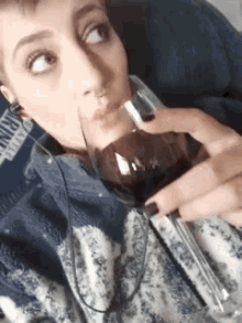 a woman is drinking a glass of wine while wearing headphones and a blue sweater .