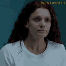 a woman with red hair is wearing a white shirt with wentworth written on the bottom right