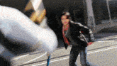 a man in a leather jacket is walking down a street