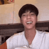 a young man is smiling and looking at the camera while wearing a white t-shirt .