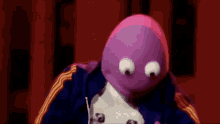 a purple puppet with big eyes is wearing a blue and yellow jacket
