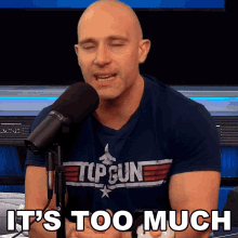a bald man wearing a top gun shirt talks into a microphone