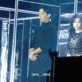 a woman stands next to a man with sara_nana written on the bottom right