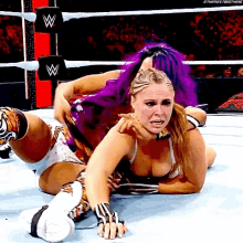 a woman with purple hair is wrestling another woman in a ring .