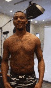 a shirtless man in ufc shorts stands in front of a camera